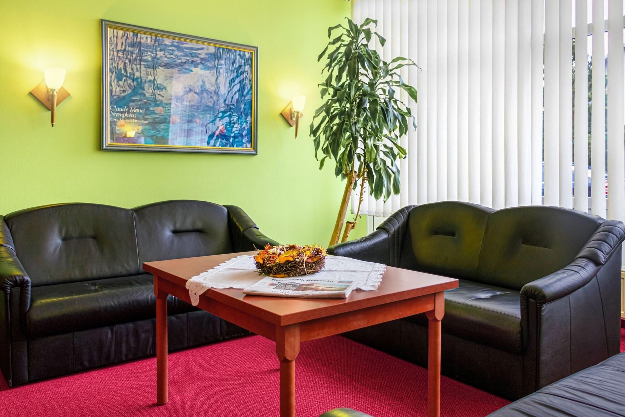 A living room with two black leather sofas, a wooden coffee table with a floral arrangement, a framed painting, and a potted plant.