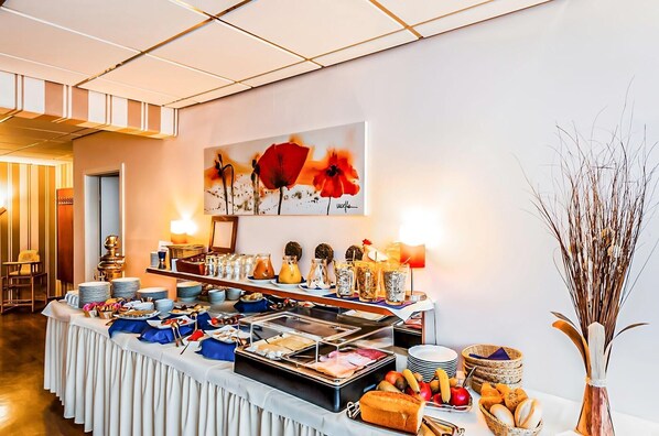 A buffet setup with various food items, a painting on the wall, and a vase with dried plants. - Hotel Muenkel (Hannover)
