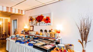 A buffet setup with various food items, a painting on the wall, and a vase with dried plants.