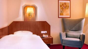 A hotel room with a bed, a nightstand with a phone, a wall-mounted lamp, and a framed picture.