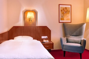 Une chambre d’hôtel avec un lit, une table de chevet avec un téléphone, une lampe fixée au mur et un tableau encadré.