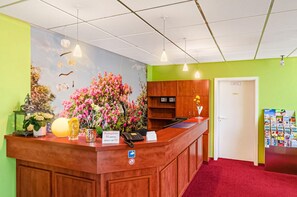 A reception desk with a floral arrangement, a phone, and a sign indicating 55 people have been selected. - Hotel Muenkel (Hannover)