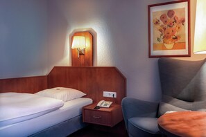 A hotel room with two beds, a nightstand with a phone, a lamp, and a framed painting on the wall. - Hotel Muenkel (Hannover)