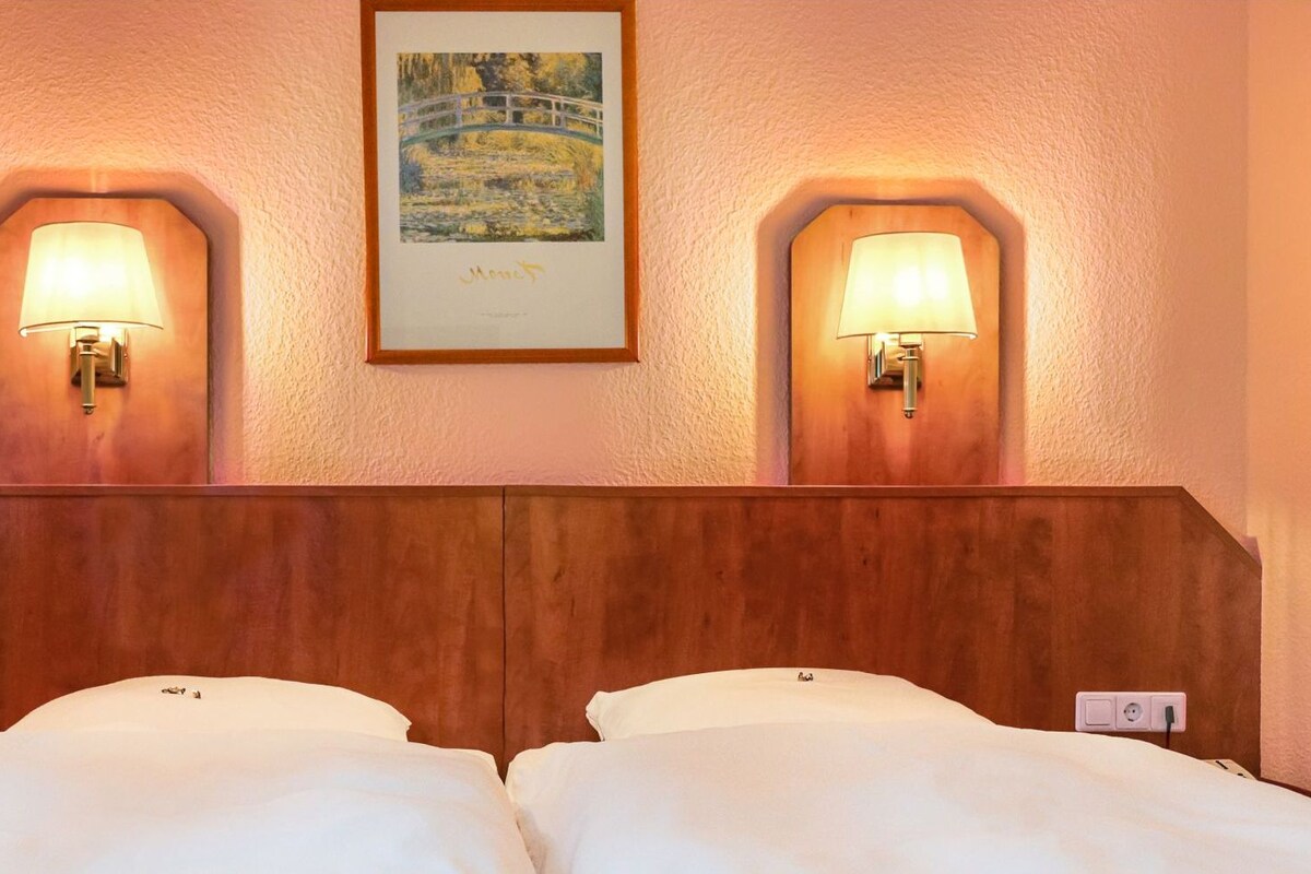A hotel room with a wooden headboard, two bedside lamps, a framed painting, and a double bed.