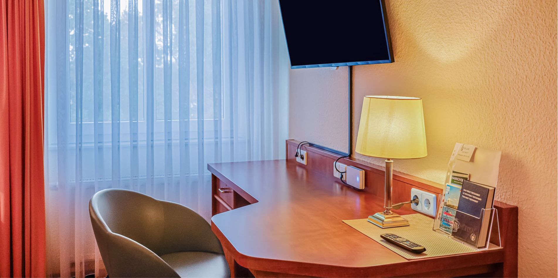 Una habitación de hotel con escritorio, silla, televisor, lámpara y ventana con persianas.