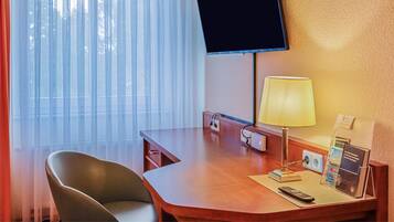 Una habitación de hotel con escritorio, silla, televisor, lámpara y ventana con persianas.