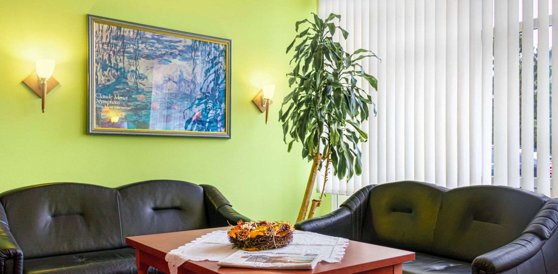 A room with two leather sofas, a wooden table with a floral centerpiece, a framed painting, and a tall plant.