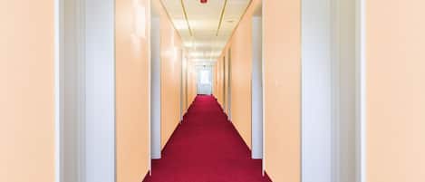 A long, narrow hallway with cream-colored walls and a red carpet.