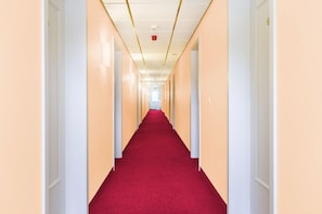Un pasillo largo y estrecho con paredes color crema y alfombra roja.