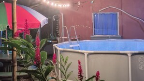 Une piscine recouverte d’une bâche bleue, entourée de plantes et agrémentée d’un parasol rouge.