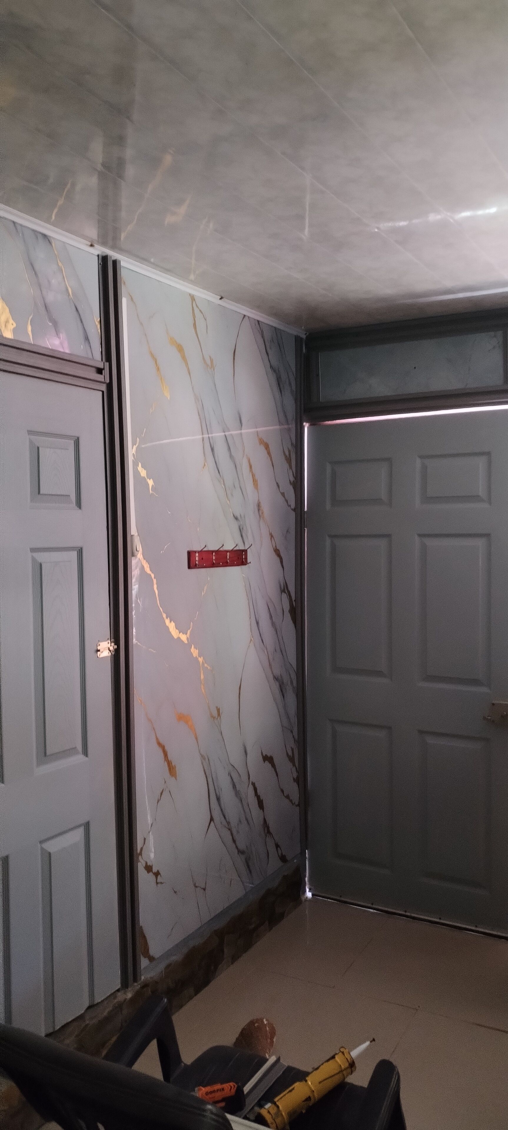 Un couloir aux murs de marbre, avec deux portes et un petit panneau rouge.