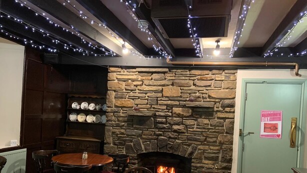 A cozy room with a stone wall, a fireplace, and string lights. There are tables and chairs for dining. - Halfway House (Blackwood)