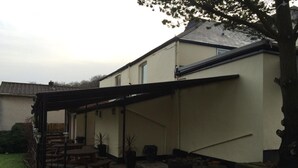 A covered patio area with a table and chairs, potted plants, and a stone wall. - Halfway House (Blackwood)