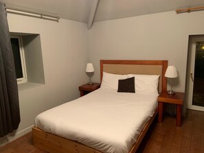 A single bed with white bedding, two bedside tables with lamps, a window with curtains, and a wooden floor. - Halfway House (Blackwood)