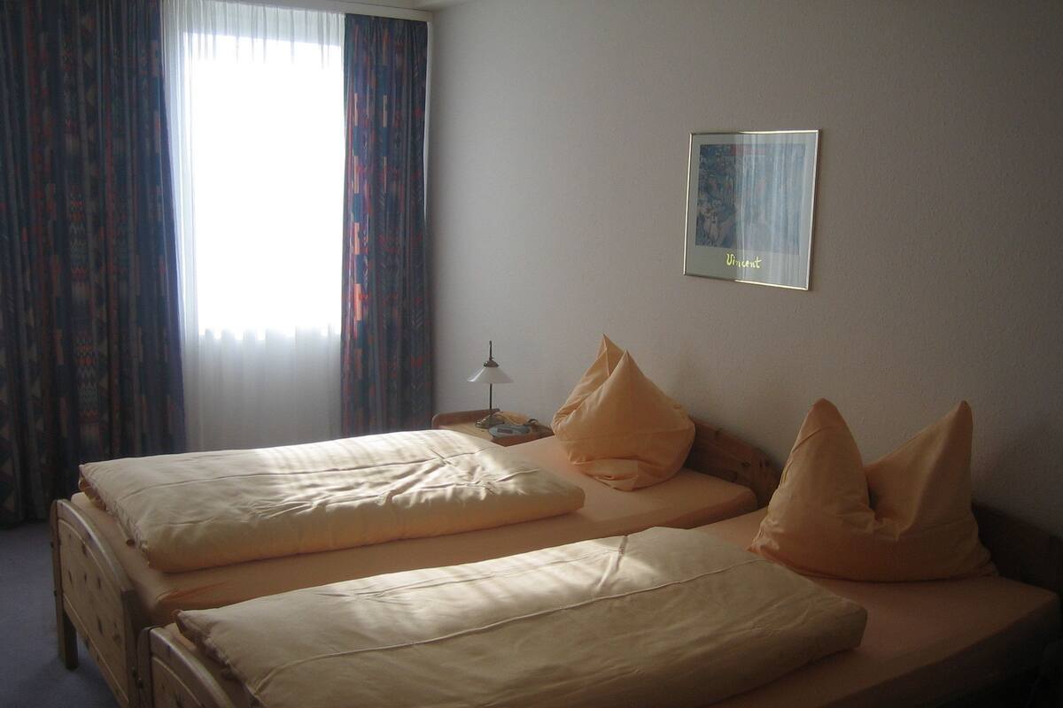 Une chambre d’hôtel avec deux lits simples, une table de chevet avec une lampe et un tableau encadré au mur.