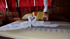 A bed with a white sheet, a heart-shaped towel arrangement, and a wooden headboard.