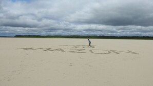 A person standing on a sandy beach with the word "MASON" written in the sand.