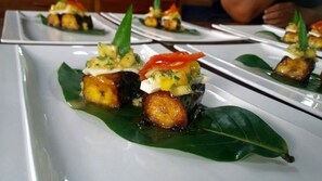 Ein Teller Essen mit einer Banane, einer Tomatenscheibe und einem Klecks Sahne auf einem Blatt.