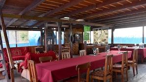 A restaurant with wooden furniture, red tablecloths, and a view of the ocean.