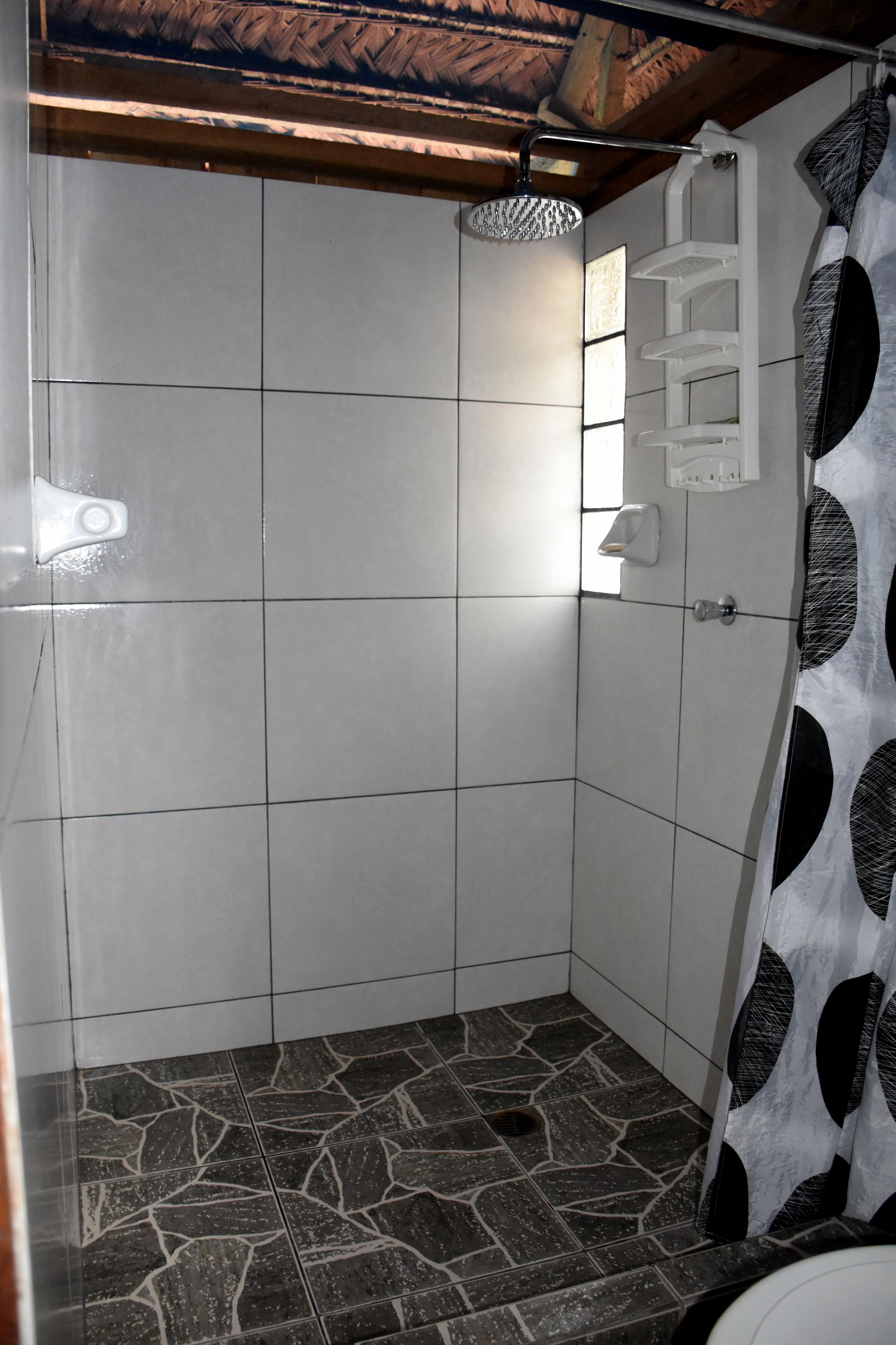 A shower area with tiled walls, a showerhead, and a patterned shower curtain.