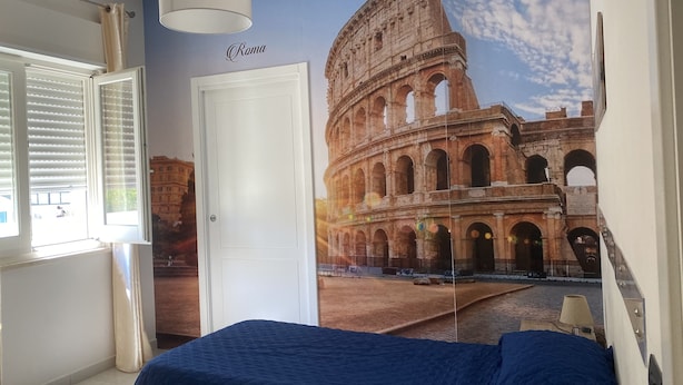 A bedroom with a large mural of the Colosseum, a white door, and a window with blinds. - B&B I Portici (Catanzaro)