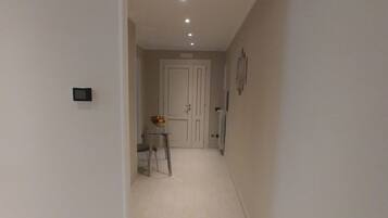 A hallway with a door at the end, a small table with a vase of flowers, and recessed lighting on the ceiling.
