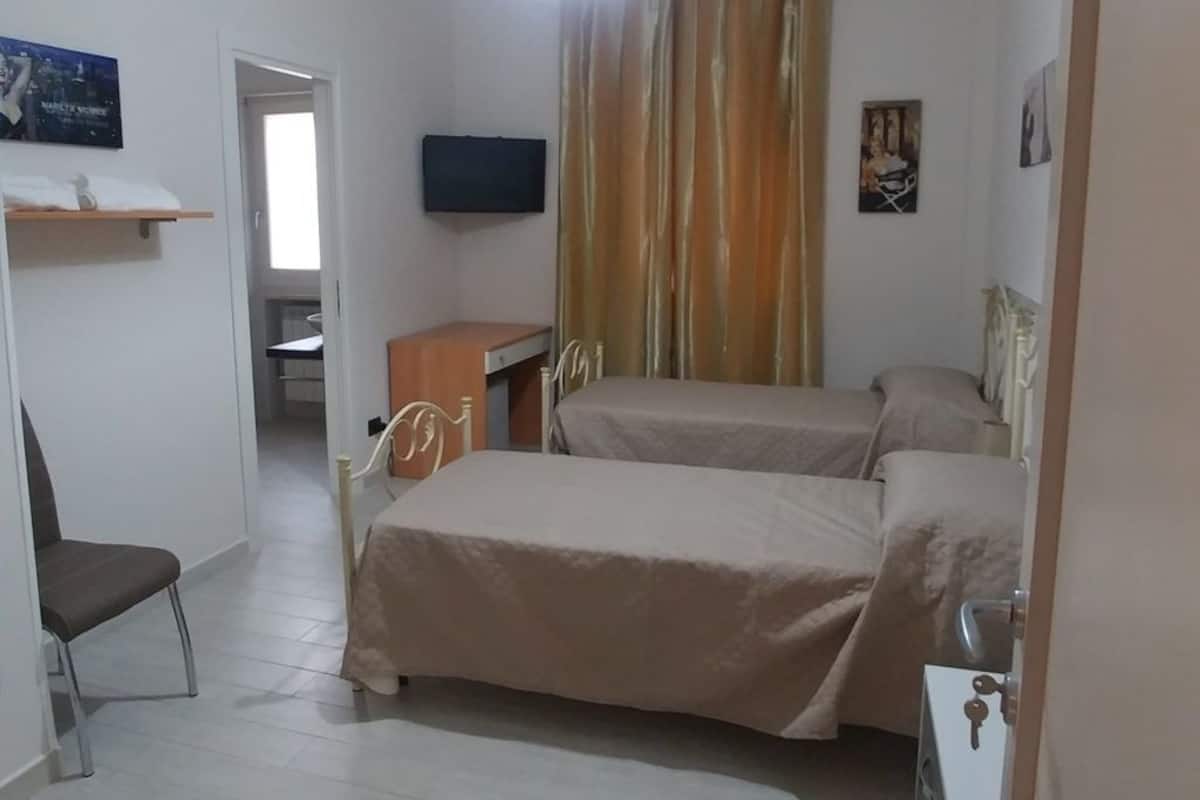A hotel room with a bed, a chair, a desk, a television, and a curtain.