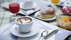A breakfast setting with a cup of coffee, a croissant, a glass of orange juice, and a bowl of fruit salad on a table. - B&B I Portici (Catanzaro)