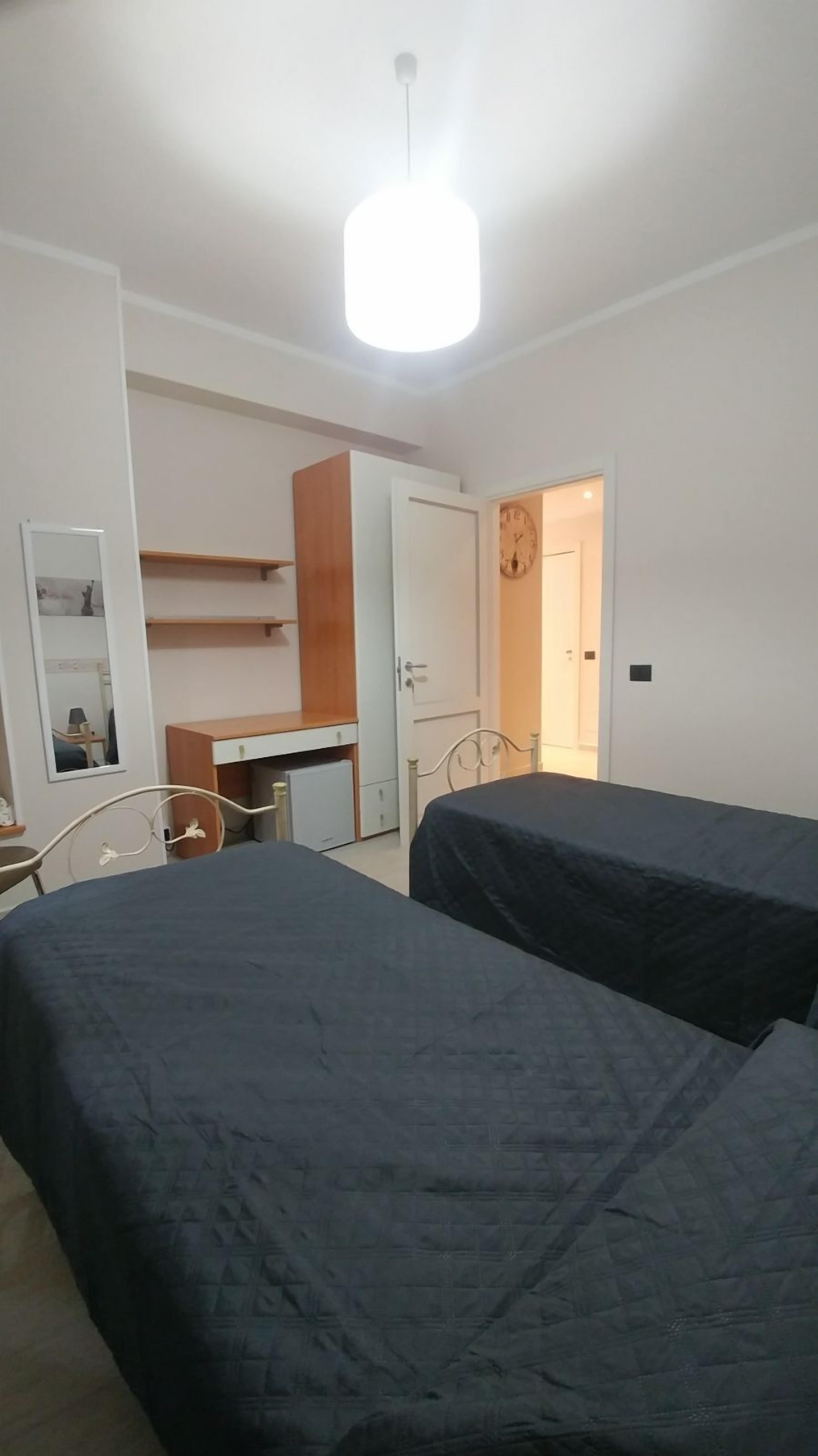 A bedroom with two beds, a desk, a wardrobe, and a mirror.