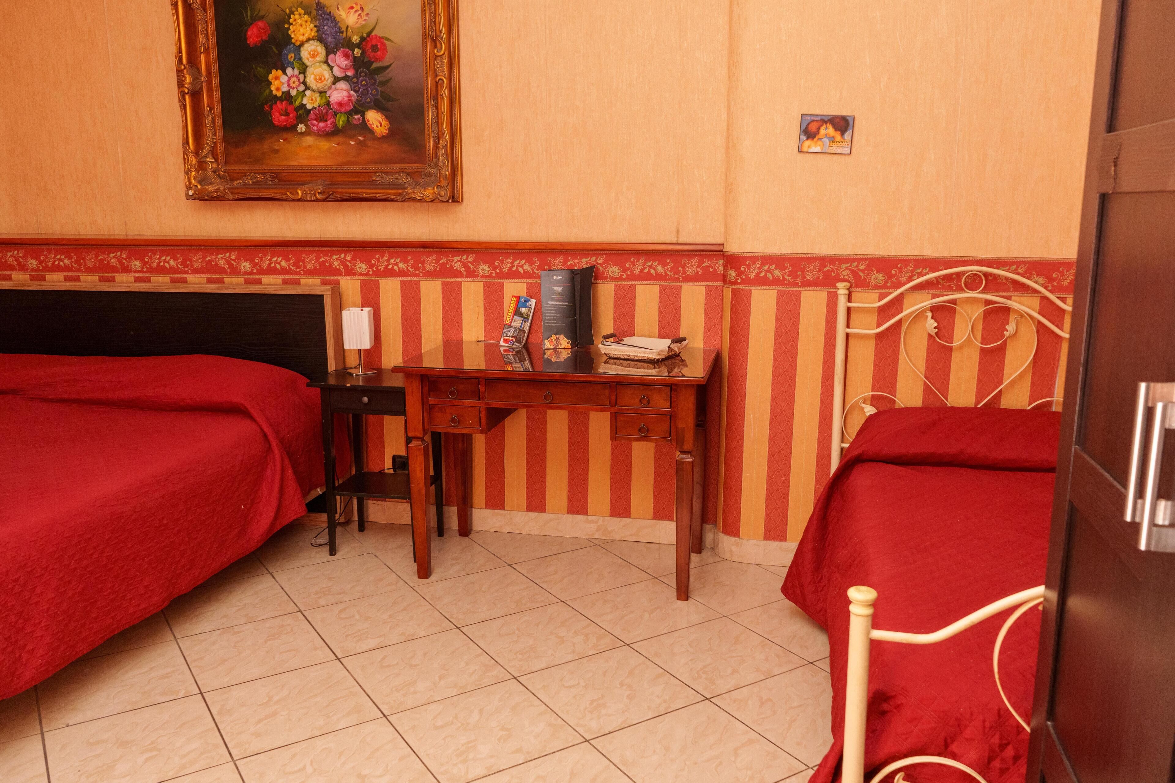Ein Hotelzimmer mit zwei Einzelbetten, einem Holztisch mit Stuhl, einem kleinen Tisch und einem Bild an der Wand.