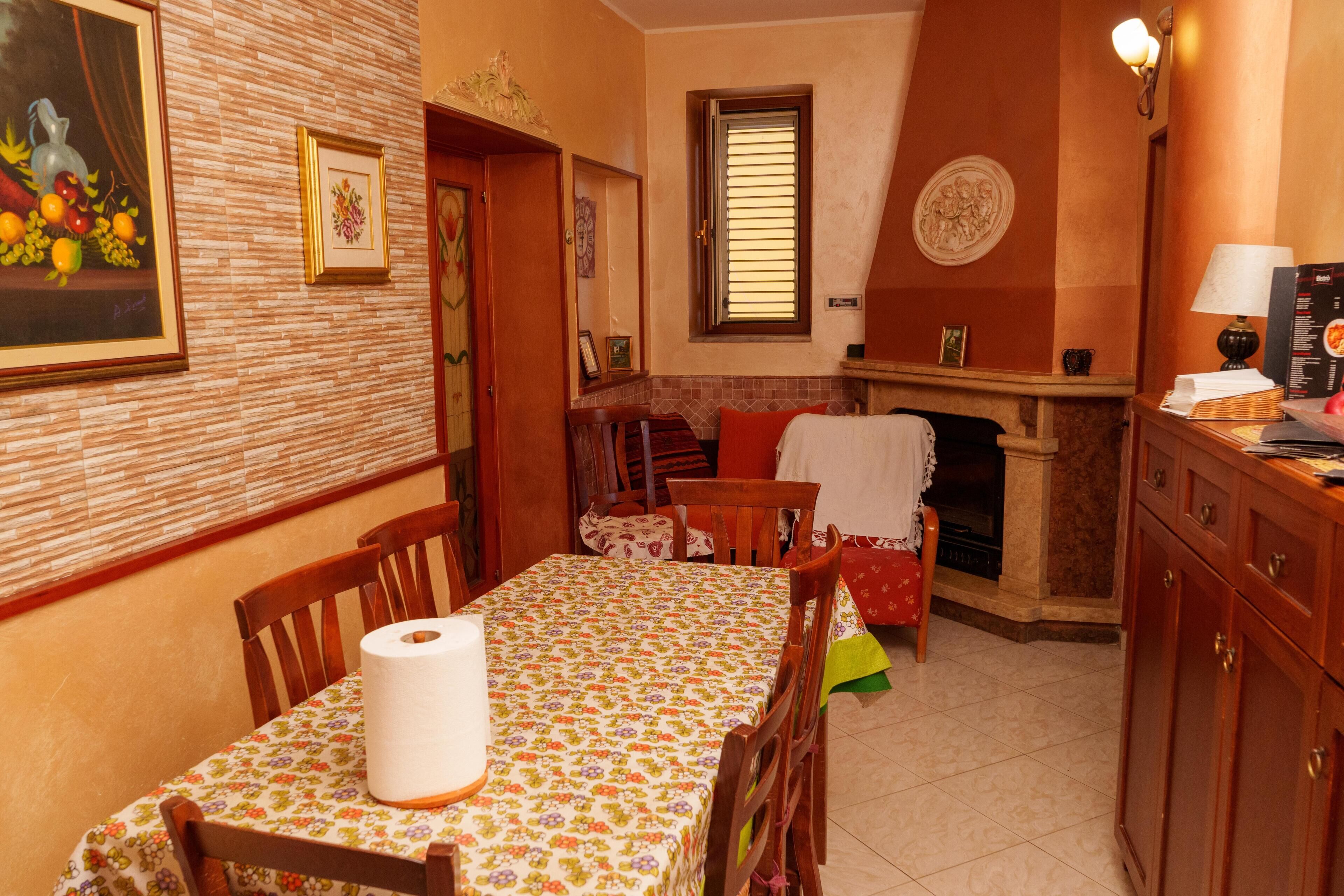 A dining area with a table set for two, a fireplace, and a kitchen area with cabinets and a countertop.