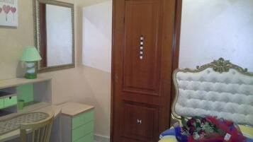 A bedroom with a bed, a desk, a chair, a wardrobe, and a mirror.