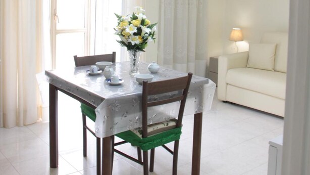 A dining area with a table set for four, a vase with flowers, and a chandelier. - Leonessa di Puglia (Altamura)