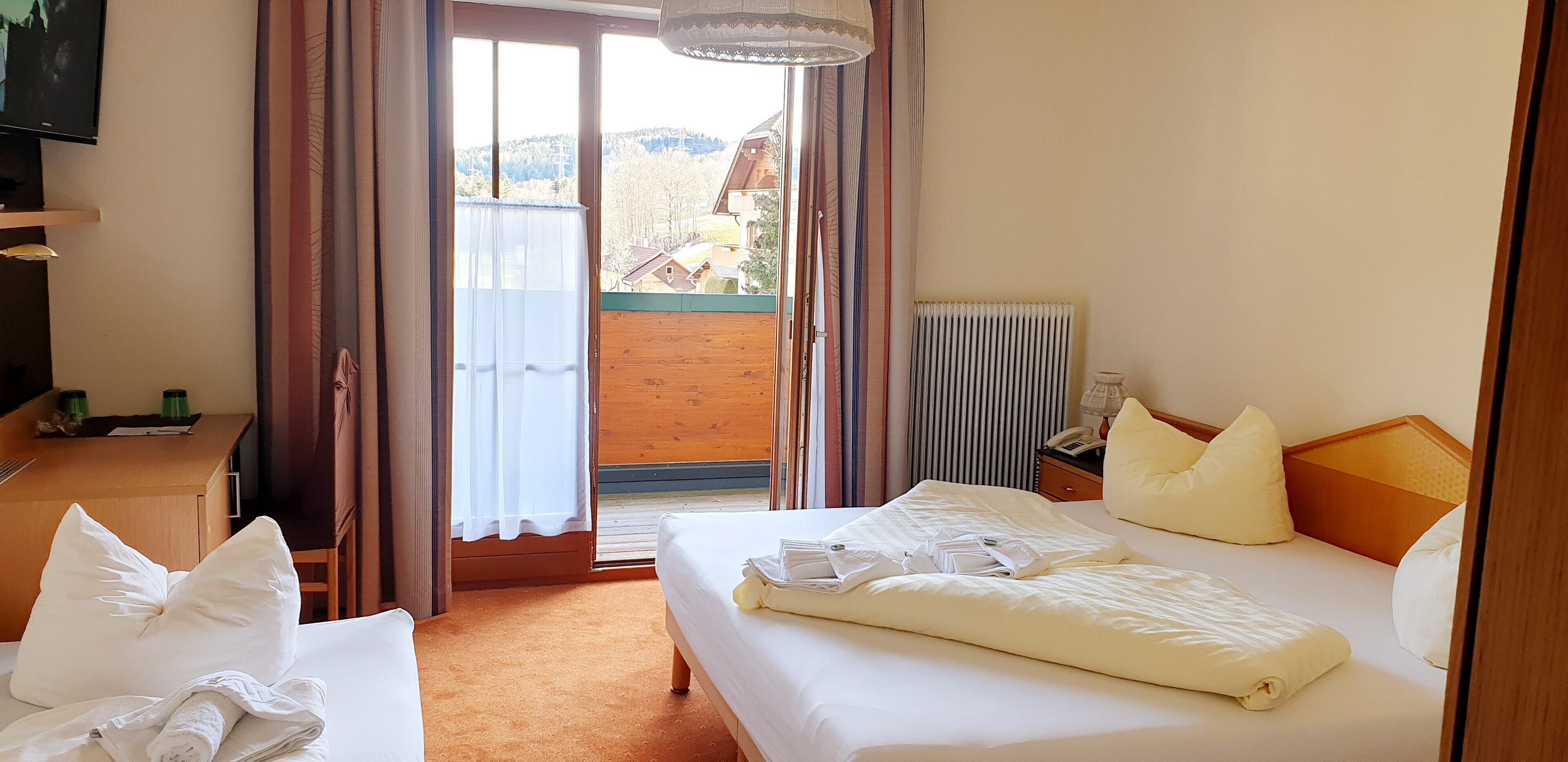 A hotel room with a bed, a desk, a chair, a radiator, and a view of the outside.
