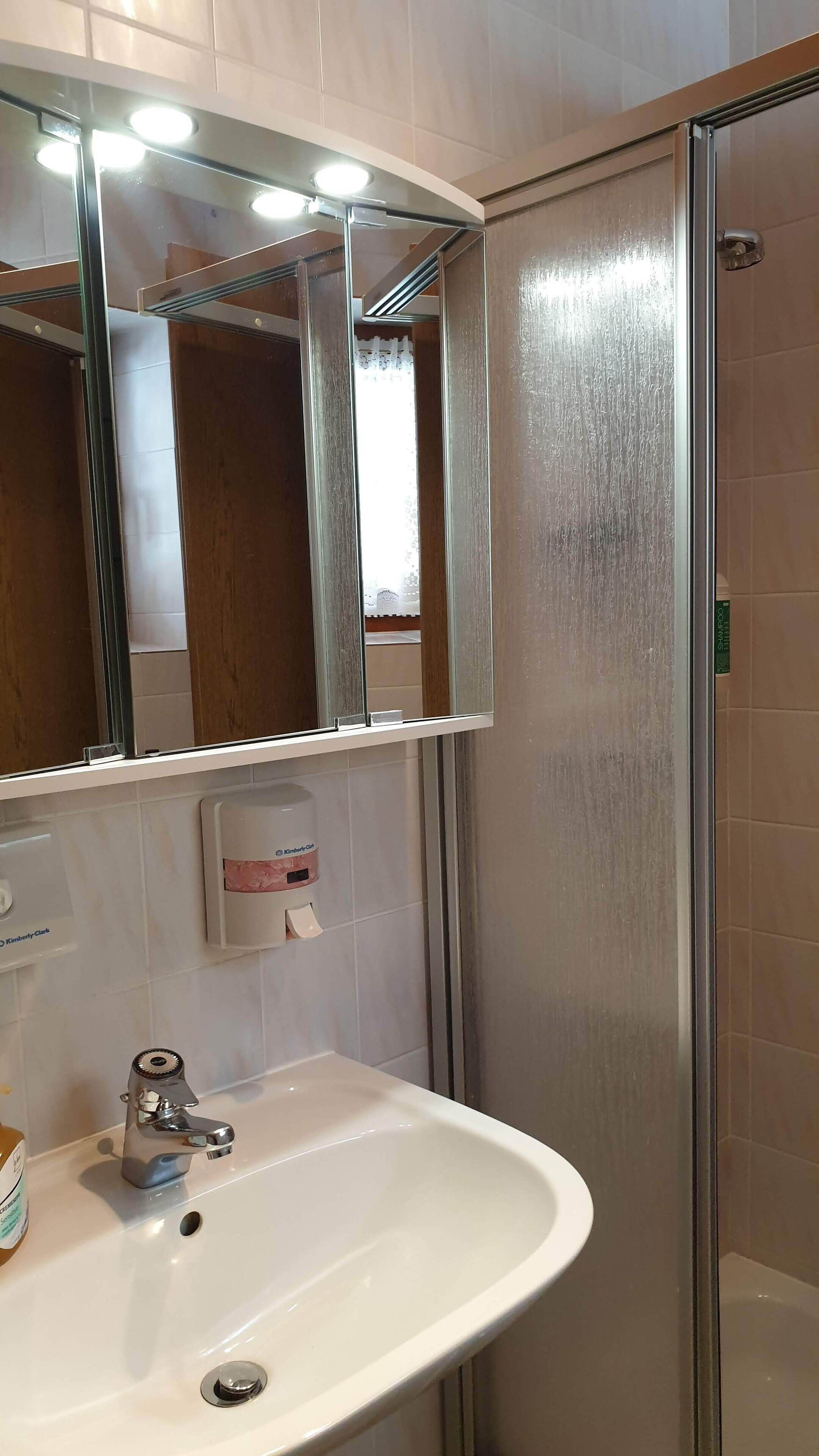 Un bagno con un lavandino bianco, uno specchio e un box doccia.