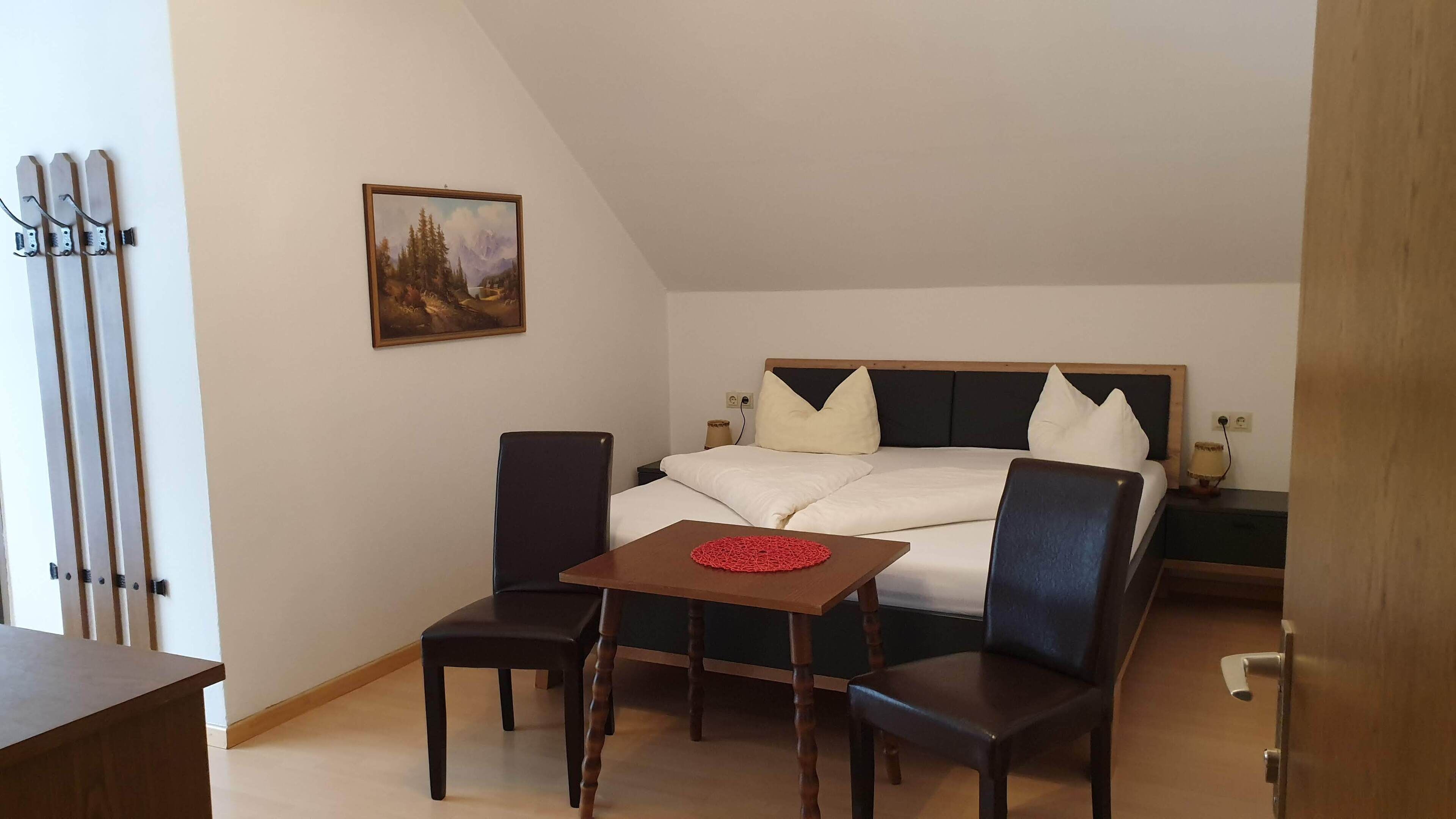 A bedroom with a bed, two chairs, a small table, a painting, and a door.