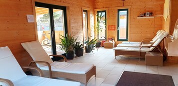 Uma cabana de madeira com duas poltronas, uma mesinha e plantas em vasos.