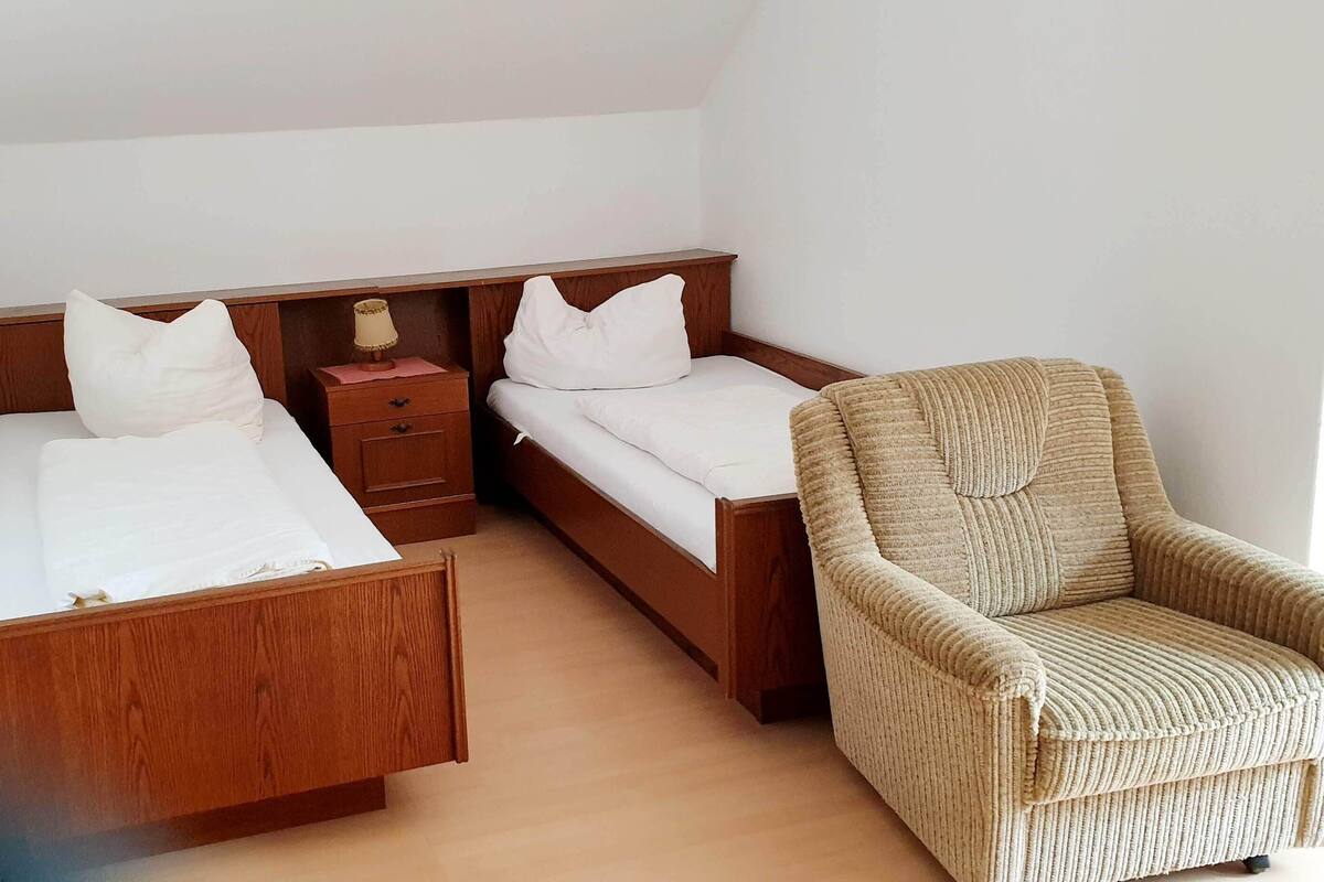 Ein Schlafzimmer mit zwei Holzbetten, einem Nachttisch, einer Lampe und einem Korbsessel.