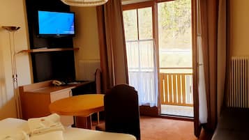 Habitación de hotel con cama, escritorio, silla, televisor y balcón con cortinas.