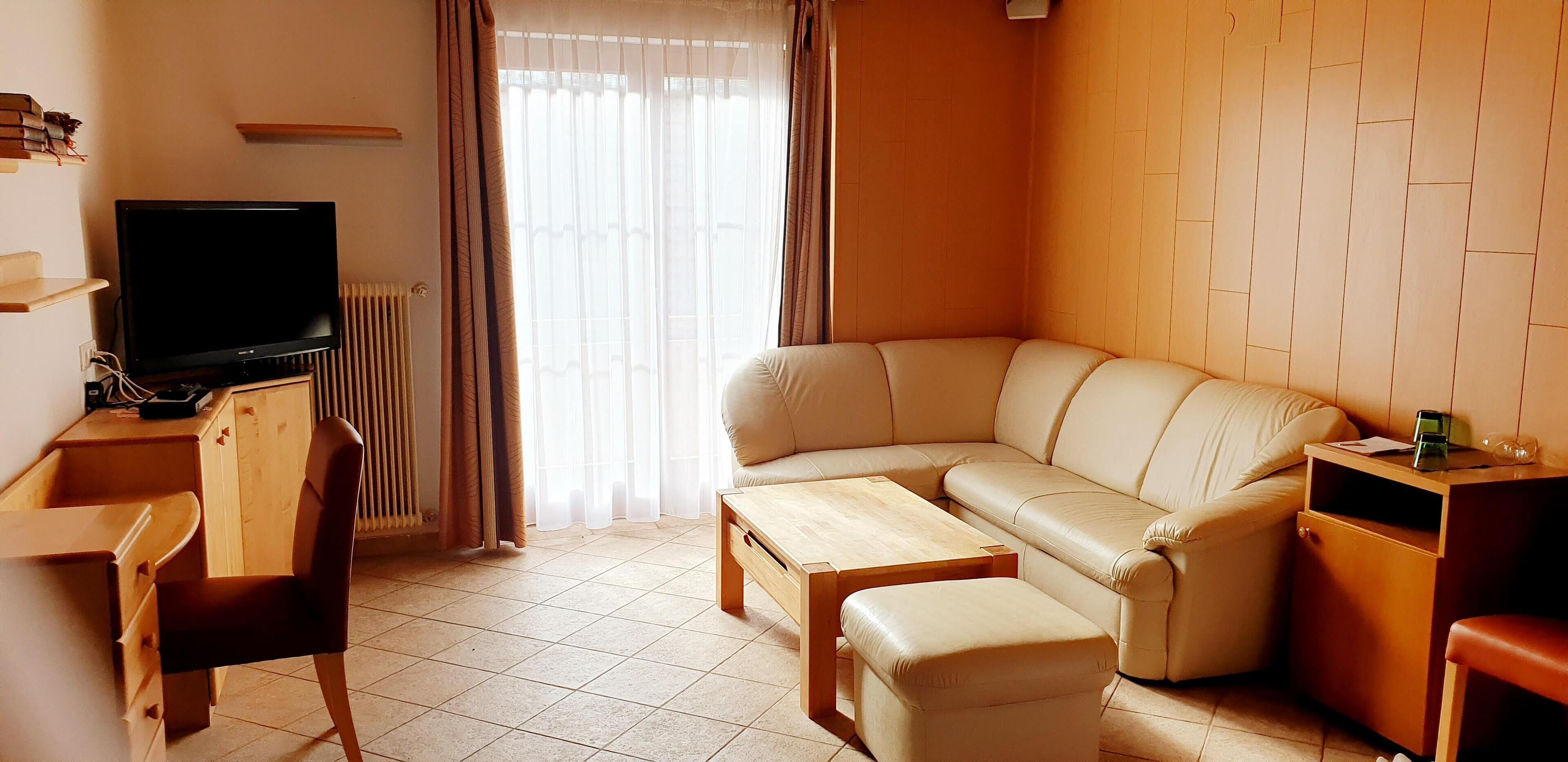 A living room with a sofa, a TV, a wooden desk, and a radiator.