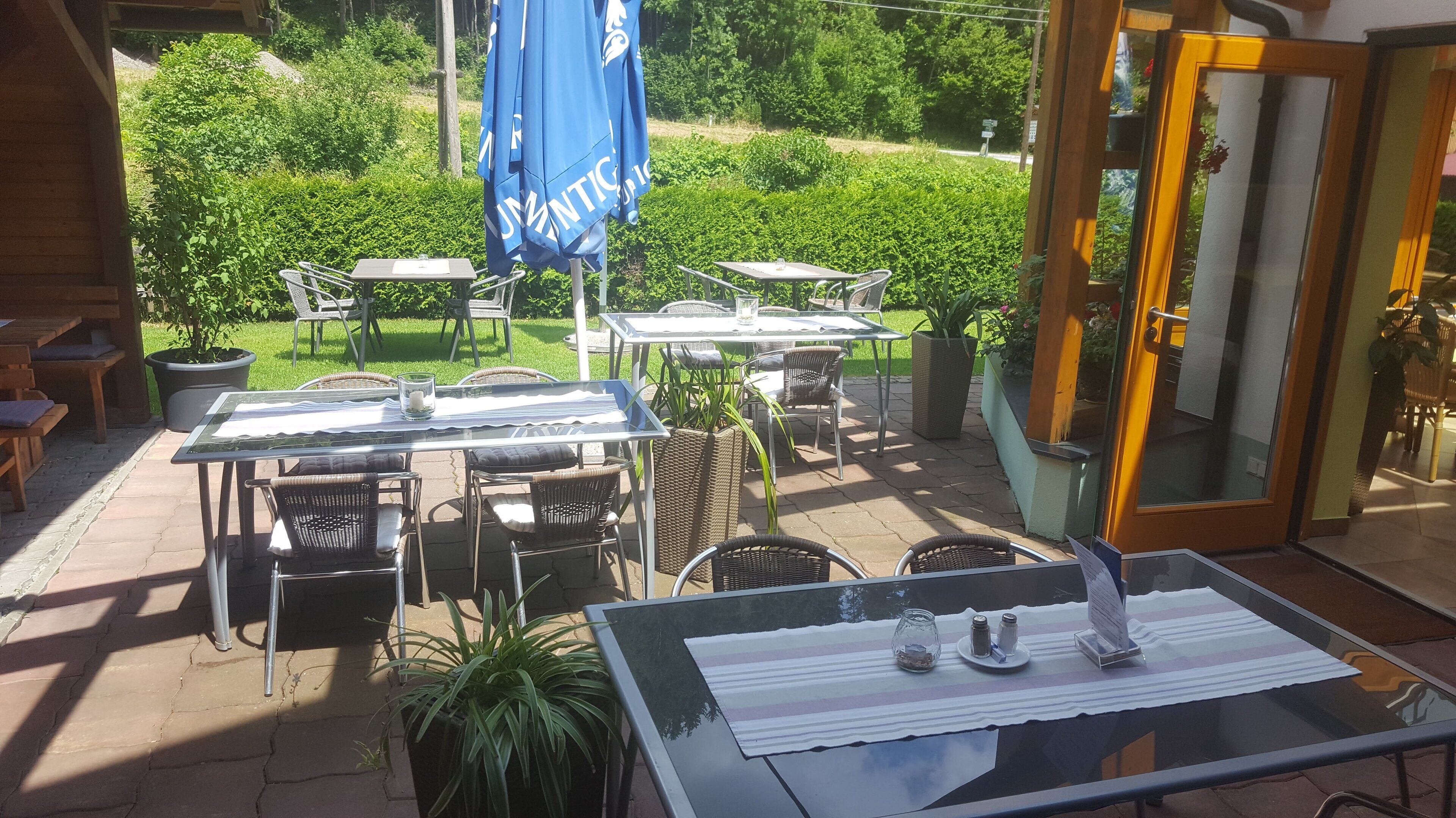 An outdoor patio with tables and chairs, a blue umbrella, and a glass door leading to the interior.