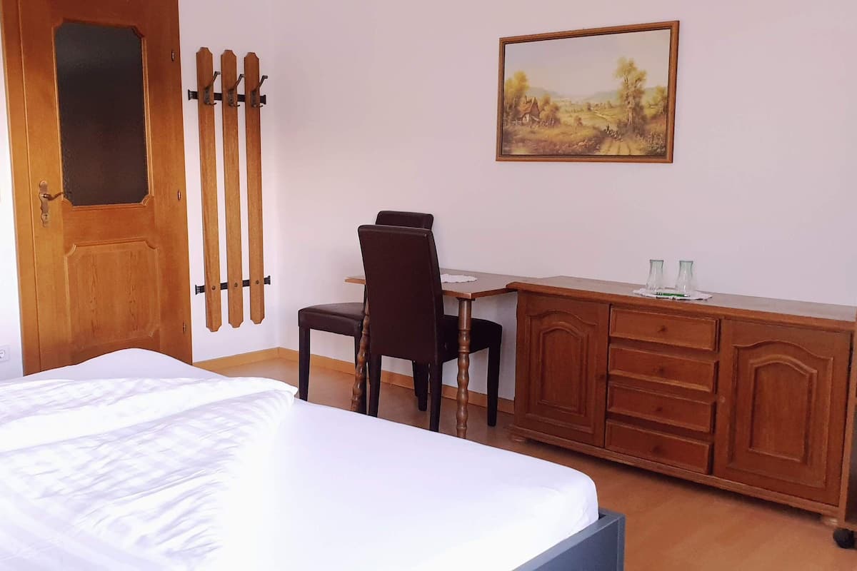 Ein Schlafzimmer mit einem Bett, einem Holztisch, einem Stuhl, einem Schrank und einem Bild an der Wand.