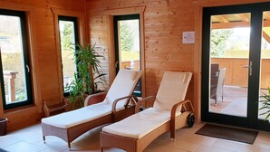 Eine Holzhütte mit zwei Korbsesseln mit weißen Kissen, einem Blumentopf und einer sichtbaren Holzterrasse durch die Glastür.