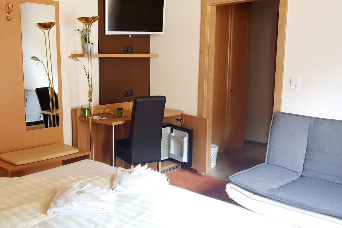 Ein Hotelzimmer mit einem Bett, einem Schreibtisch mit Stuhl, einem Fernseher, einem Spiegel und einem Sofa.