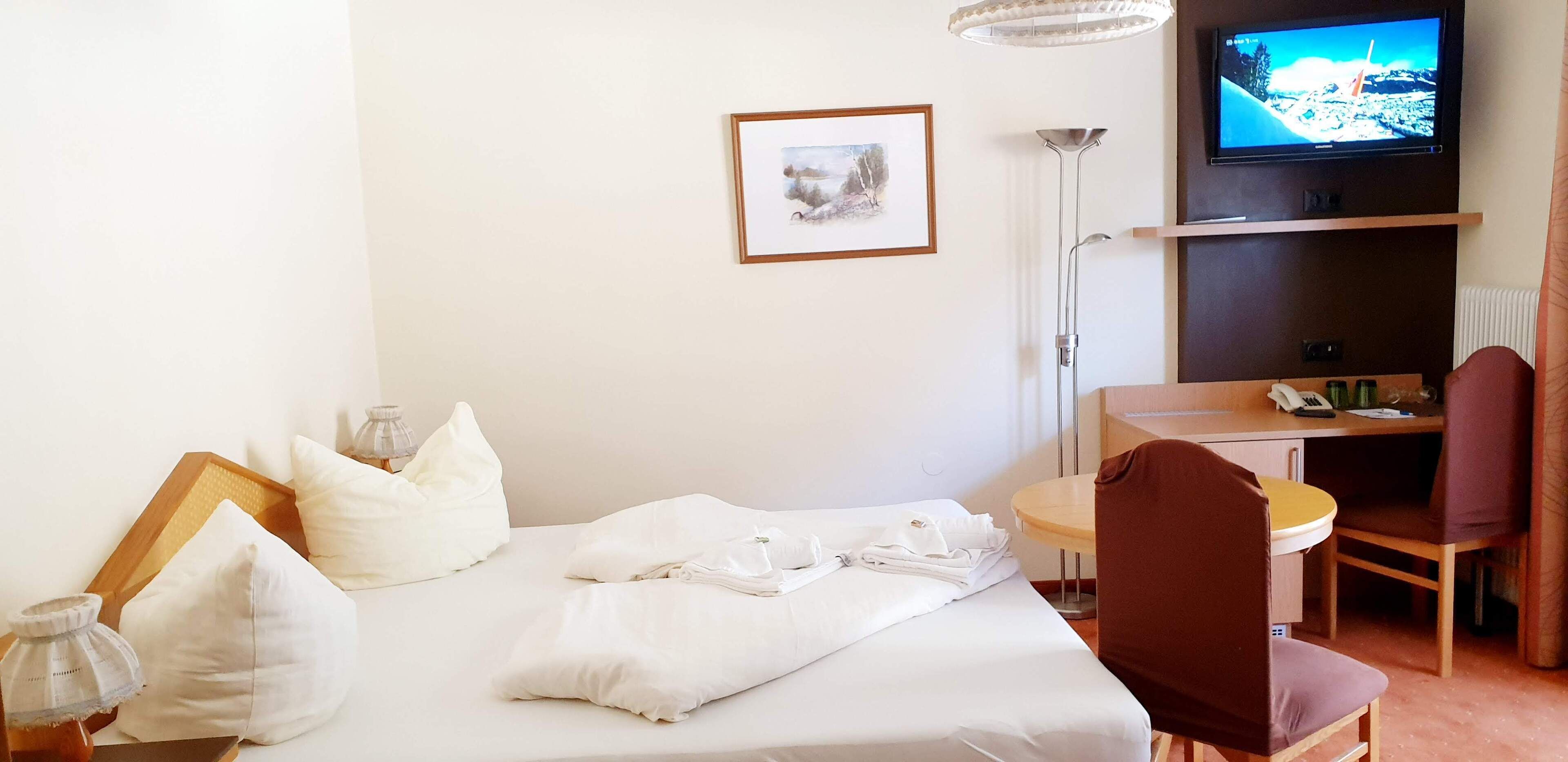 Una habitación de hotel con una cama, un escritorio, una silla, un televisor y un cuadro en la pared.