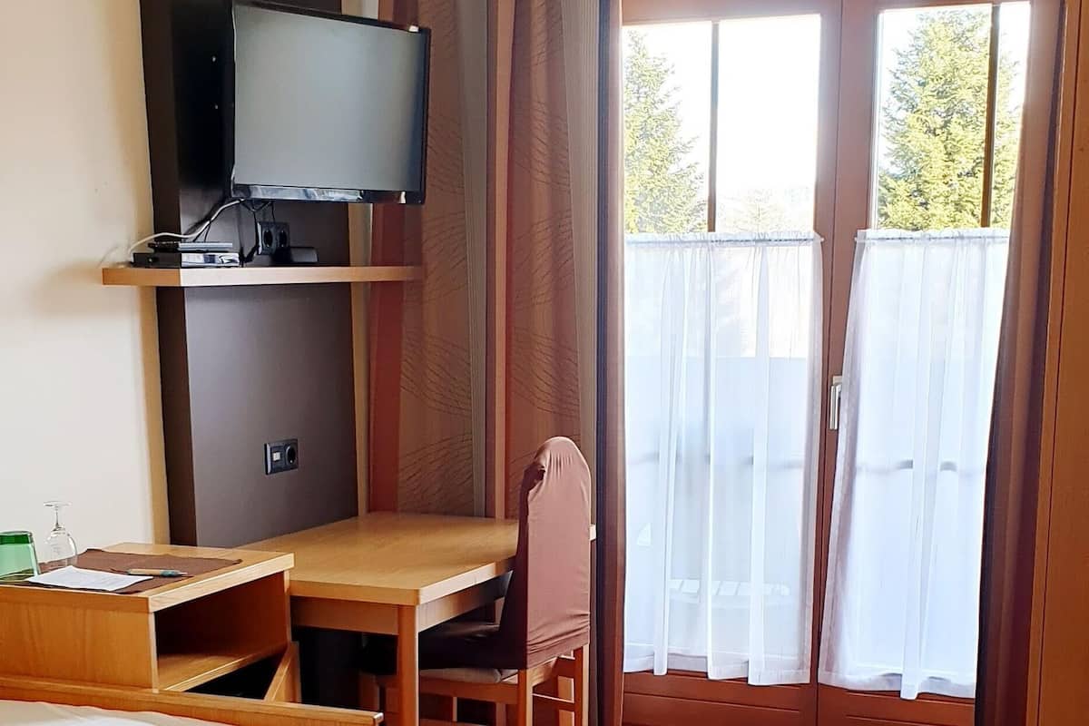 Ein Hotelzimmer mit einem Bett, einem Schreibtisch mit Stuhl, einem Fernseher und einem großen Fenster mit Vorhängen.