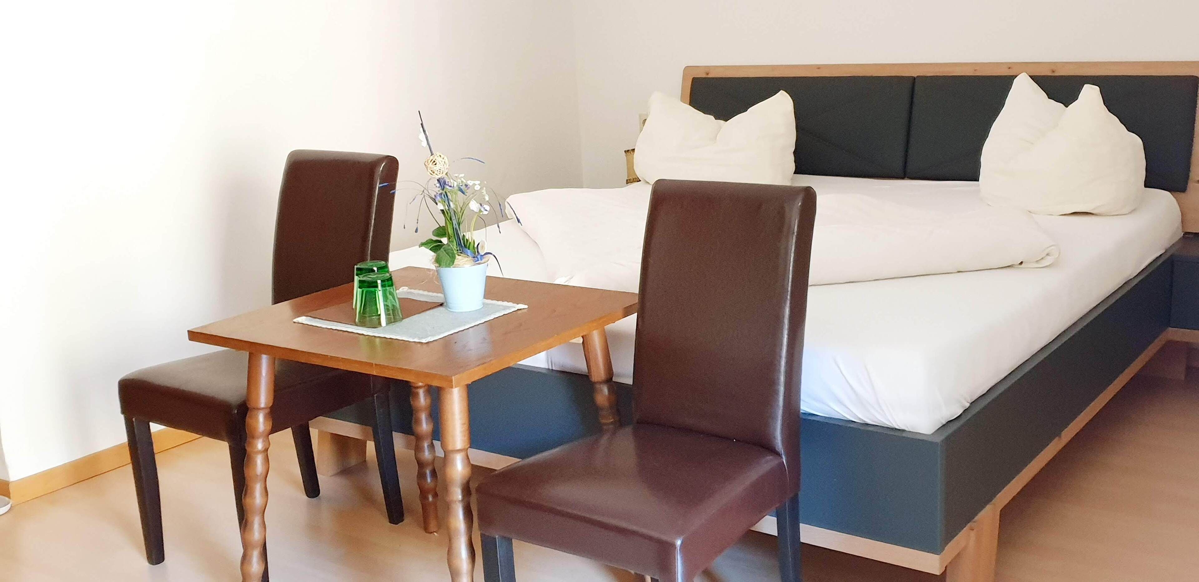 A hotel room with a bed, two chairs, a small table, and a potted plant.