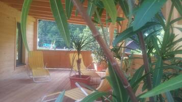 Una terraza de madera con dos sillas amarillas y una mesa, rodeada de plantas en macetas.
