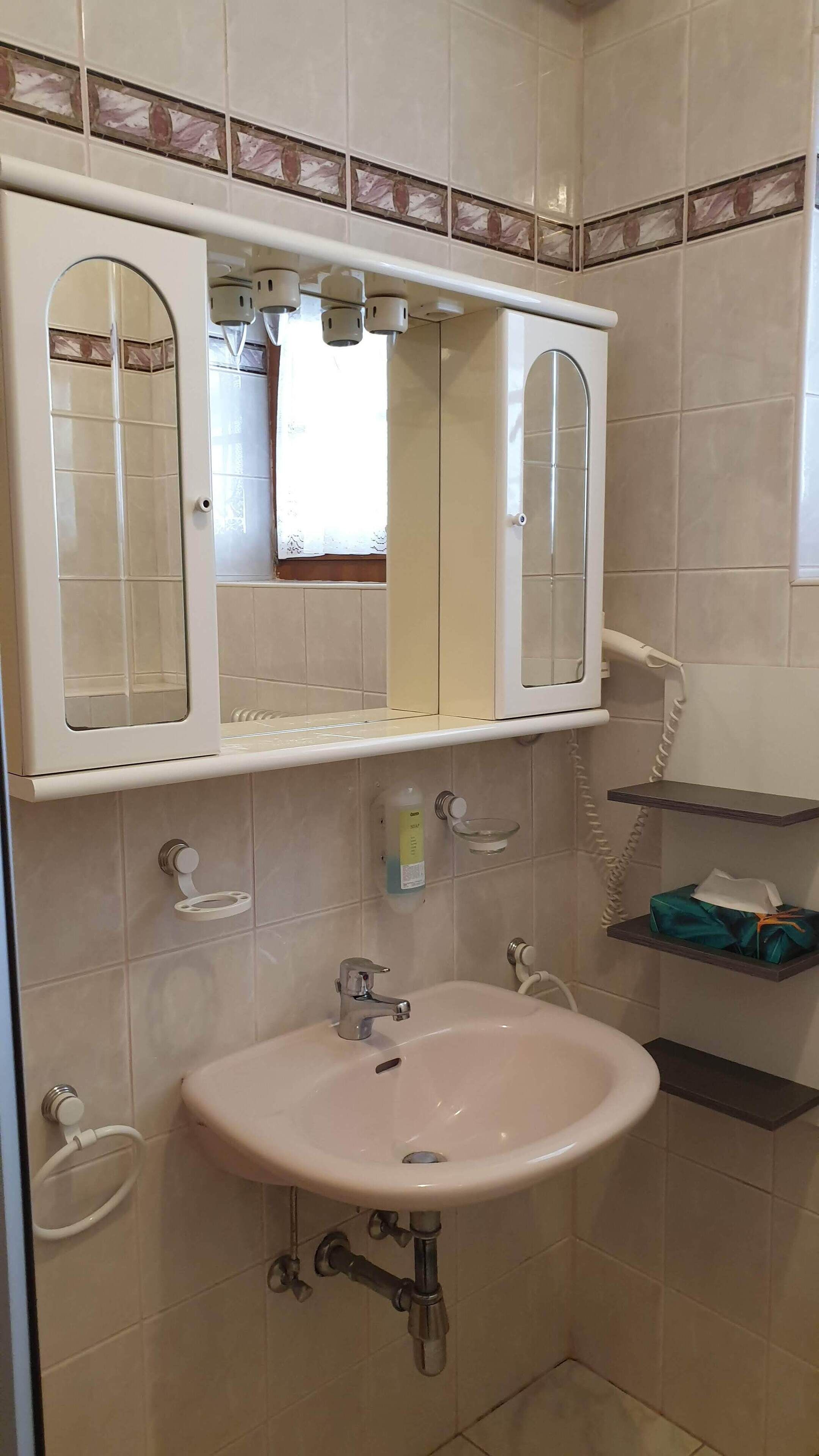 Un baño con un lavabo blanco, un espejo encima y un teléfono sujeto a la pared.