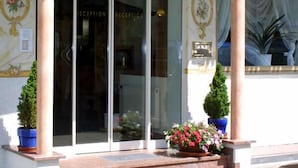 A hotel entrance with a reception desk, glass doors, and a decorative archway. - Hotel garni Schmideler (Sonthofen)